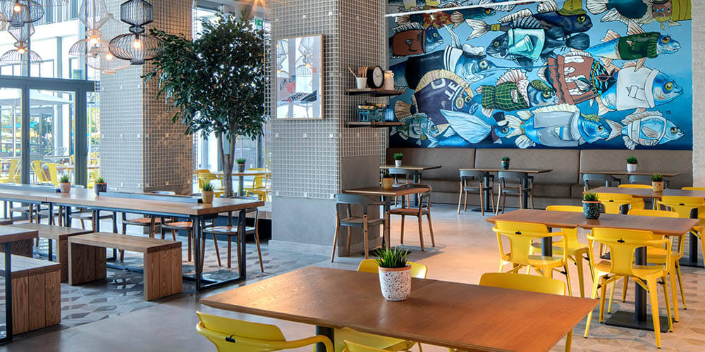 Guests enjoying brunch at The Daily within Rove Hotel, featuring modern minimalist seating, natural light, and open buffet serving area