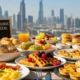 A vibrant table filled with an affordable brunch spread, including pancakes, scrambled eggs, bacon, and pastries, with the Dubai skyline and the Burj Khalifa visible in the sunlit background.
